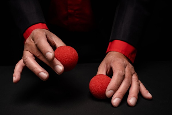 Die Hände eines Zauberers mit zwei roten Bällen.