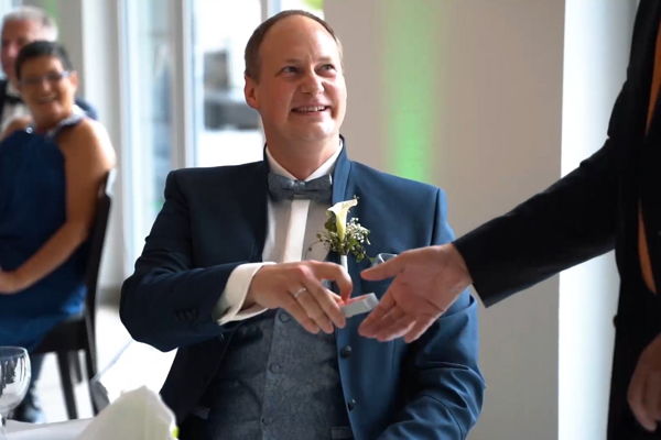 Der lächelnde Bräutigam bei einem Zaubertrick mit Spielkarten bei seiner Hochzeit.