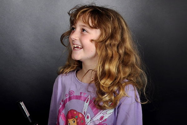 Ein Mädchen mit dunkelblonden Haaren und einem lila Pullover lacht nach einem Zaubertrick.