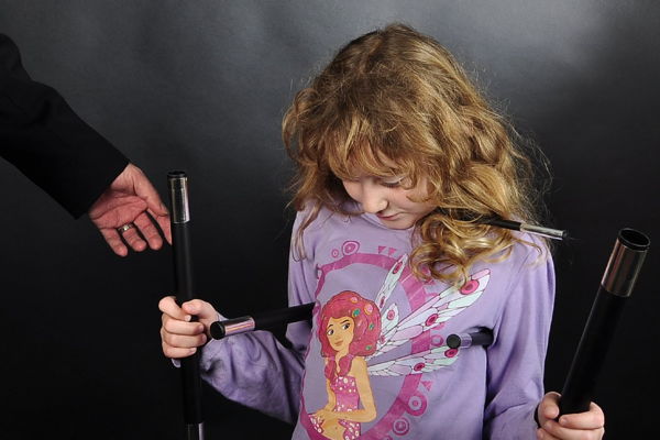 Ein Mädchen mit lockigen dunkelblonden Haaren und einem lila Pullover hält verschiedene Zauberstäbe in der Hand.