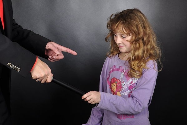 Ein Mädchen mit lockigen dunkelblonden Haaren und einem lila Pullover assistiert einem Zauberer bei einer Zauberei auf einem Kindergeburtstag.