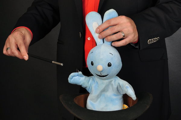 Ein Zauberer zaubert bei einem Kindergeburtstag ein blaues Stoffkaninchen aus einem Hut.