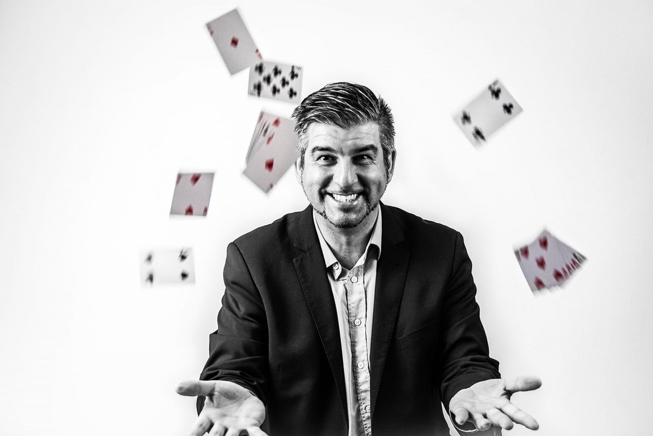 Schwarzweiß-Portrait des Zauberkünstlers Michele Augusta mit Spielkarten.